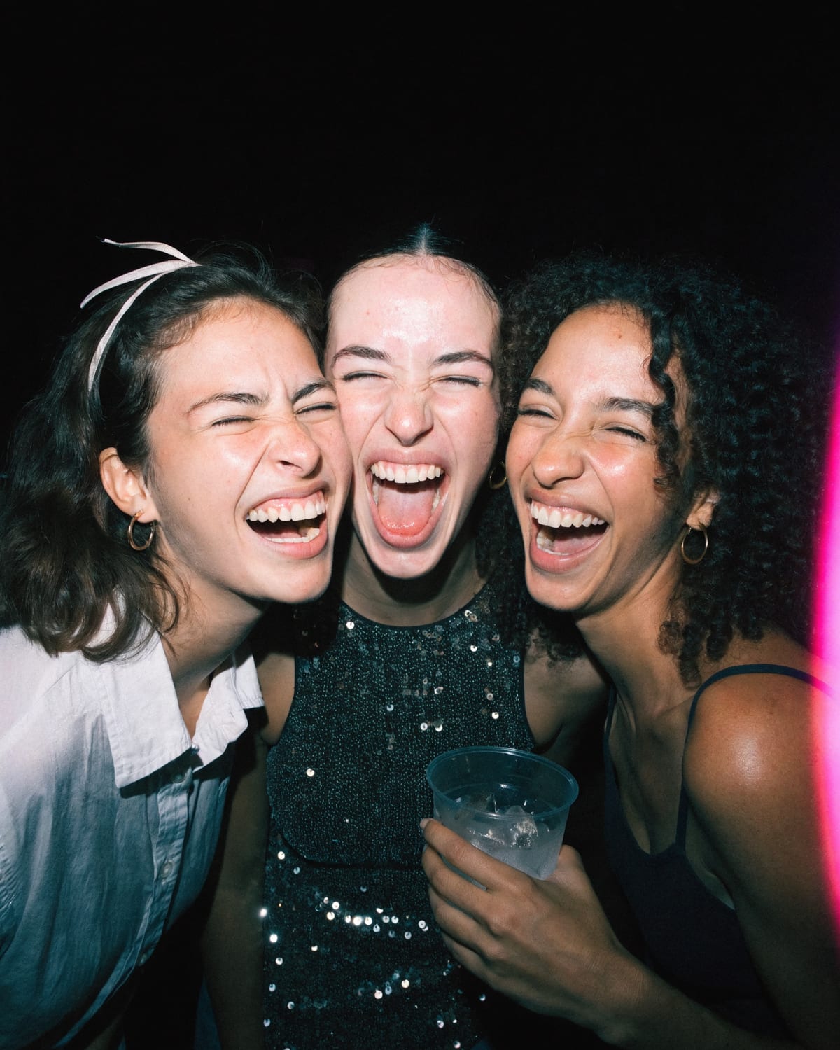 Three friends laughing together under a camera flash on a night out